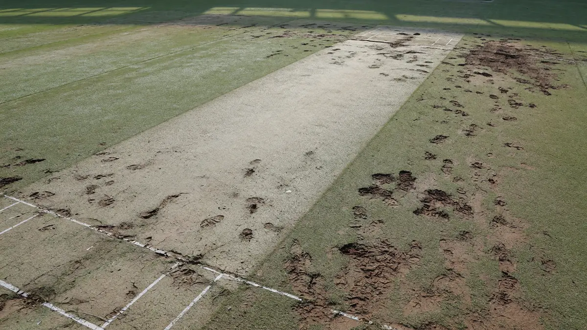 Editorial photograph of a cricket pitch close-up showing rough patches and bowler footmarks outside the right-hander's off-stump on the Chinnaswamy surface